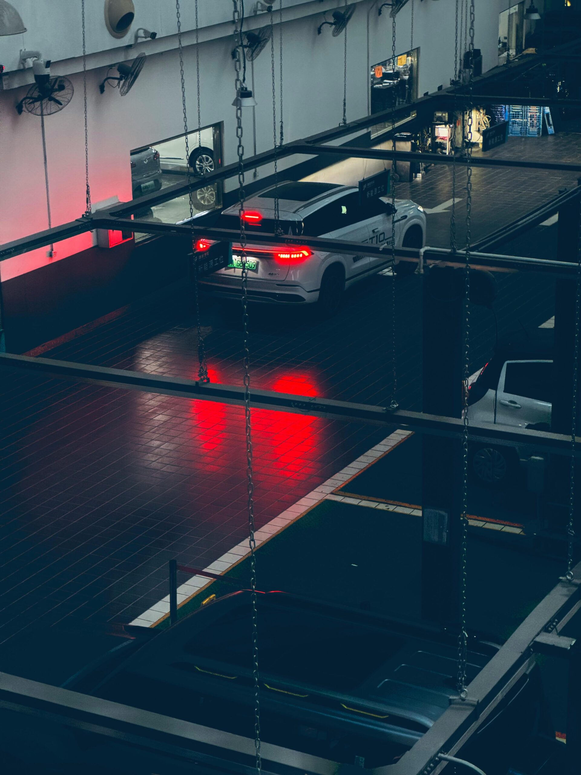 A sleek white car parked indoors reflecting red lights in a dark parking structure.