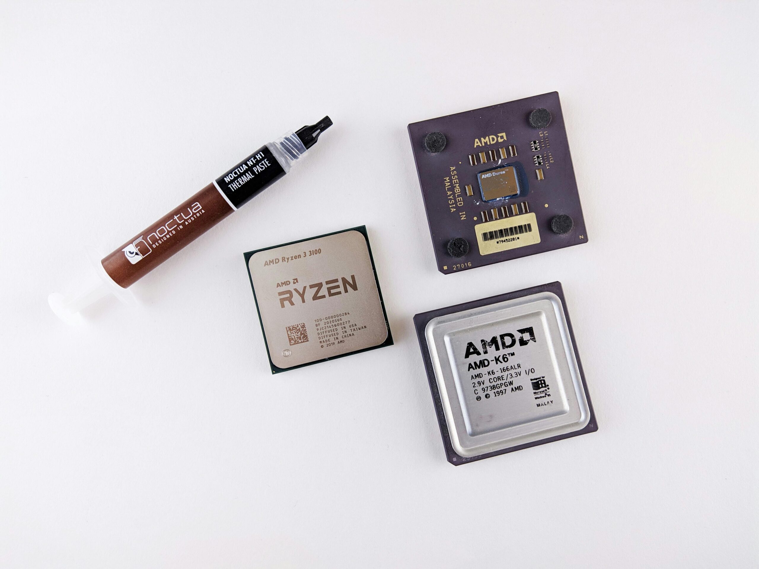 High-angle view of AMD processors and Noctua thermal paste on a white surface.