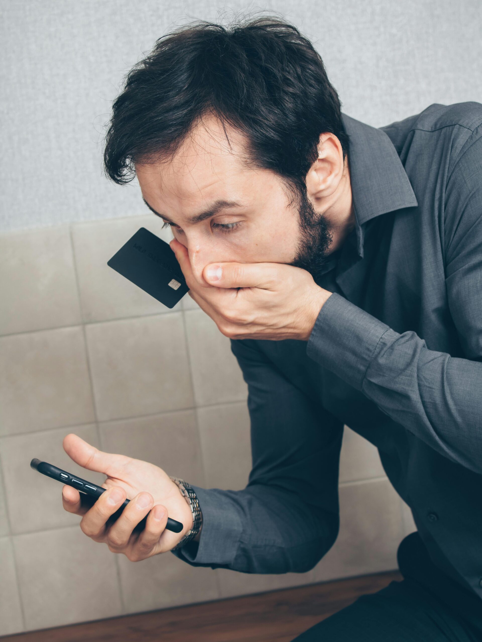 Man in shock discovering possible fraud or data breach with smartphone and credit card.